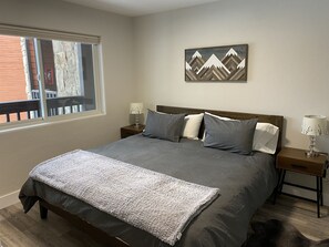 A bedroom with a large bed, two bedside tables, a window, and a wall-mounted artwork.