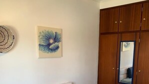 A bedroom with a bed, two pillows, a wooden wardrobe, a mirror, and a wall art piece. - Almograve House (Almograve)