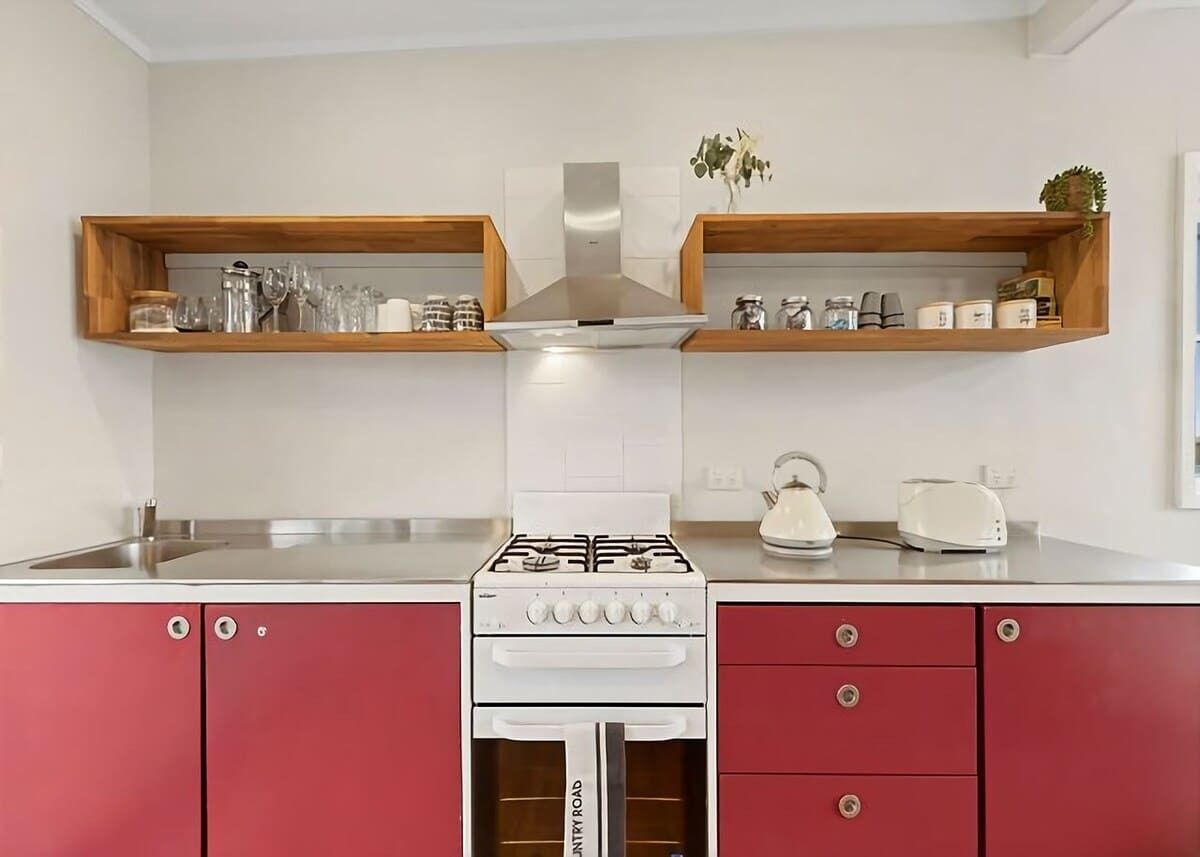 A kitchen with a gas stove, oven, and two wooden shelves above the countertop.