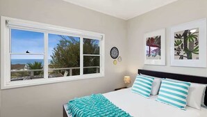 A bedroom with a bed, a window with a view, and two framed pictures on the wall. - Lil Sea Shack by the Sea (Malua Bay)