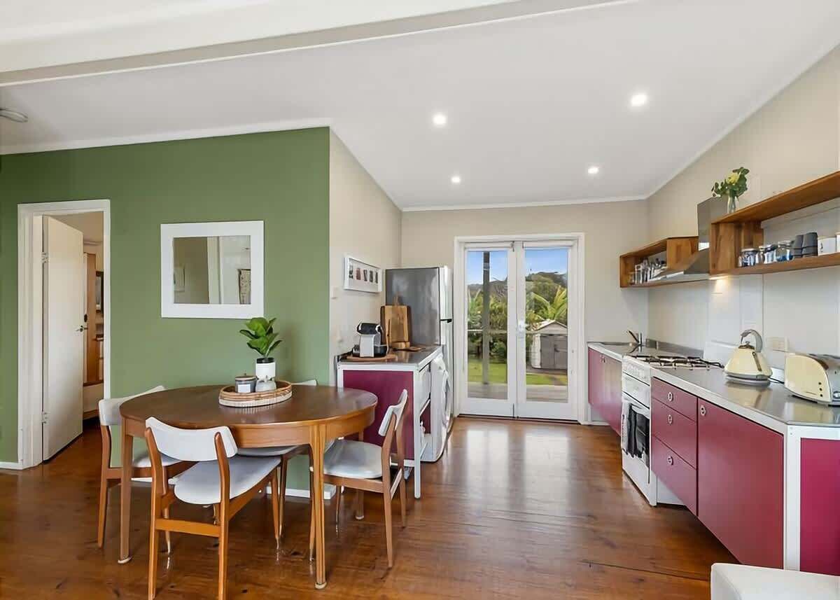A modern kitchen with a dining area, wooden flooring, and a view through glass doors.
