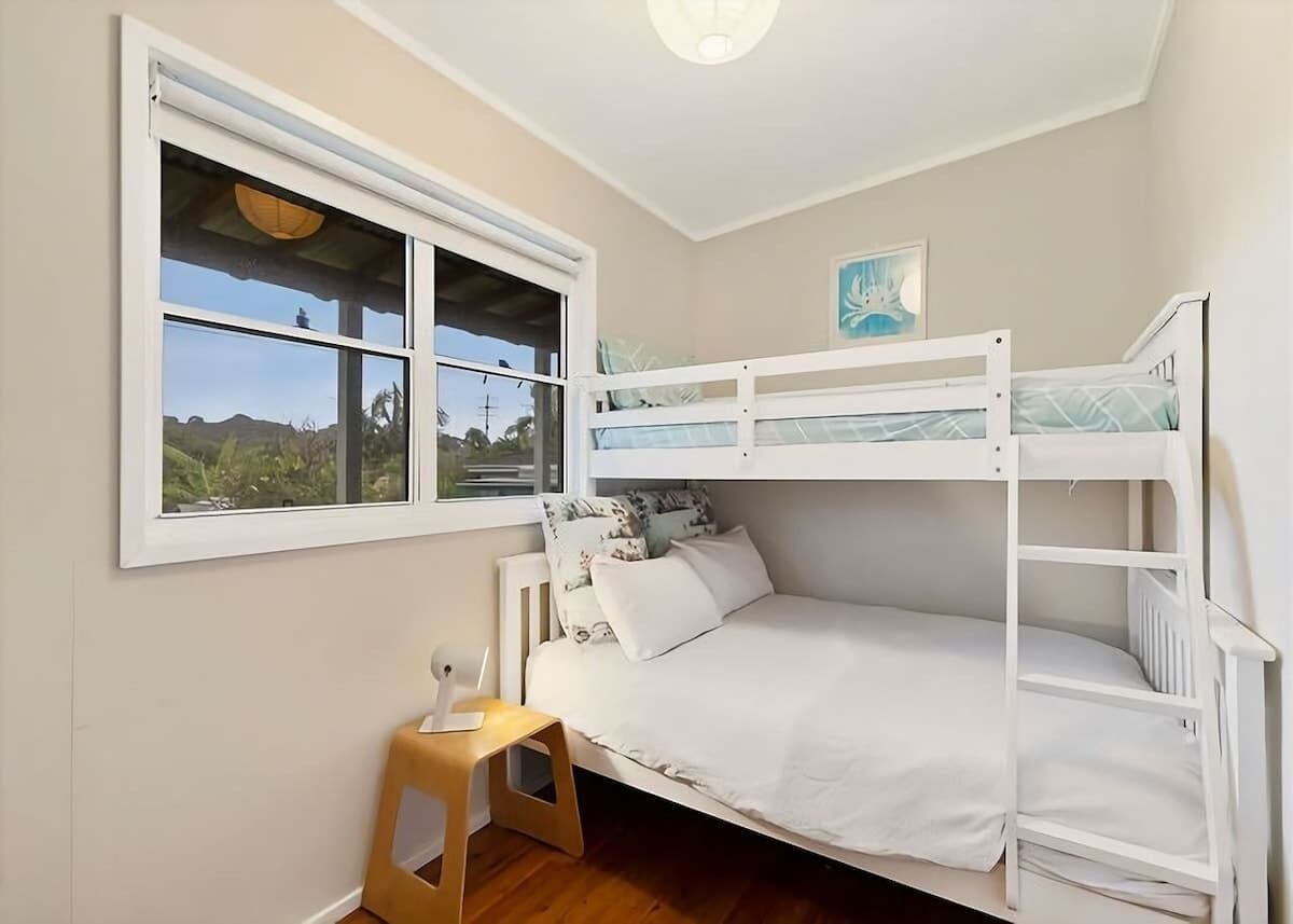 Une chambre avec un lit superposé, une fenêtre, un petit tabouret et un tableau accroché au mur.