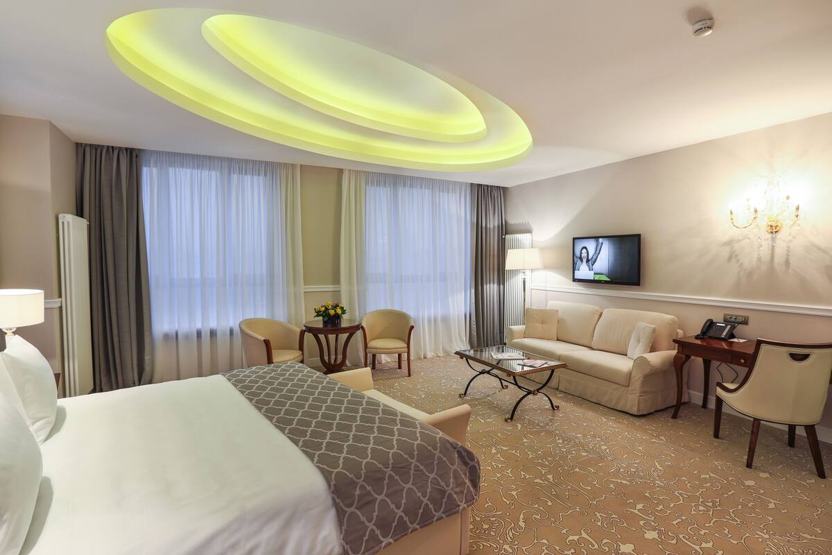 Een hotelkamer met een bed, twee fauteuils, een bank, een salontafel, een televisie en een lamp.