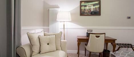 A hotel room with a bed, a desk, a chair, a lamp, and a painting on the wall.
