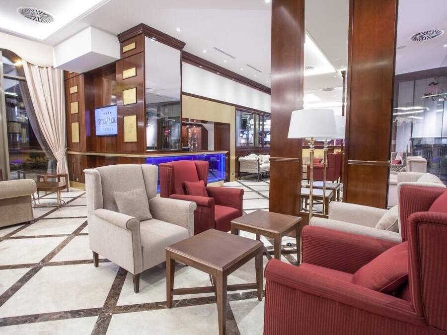A hotel lobby with a modern design, featuring a mix of seating areas, a reception desk, and a visible TV screen.