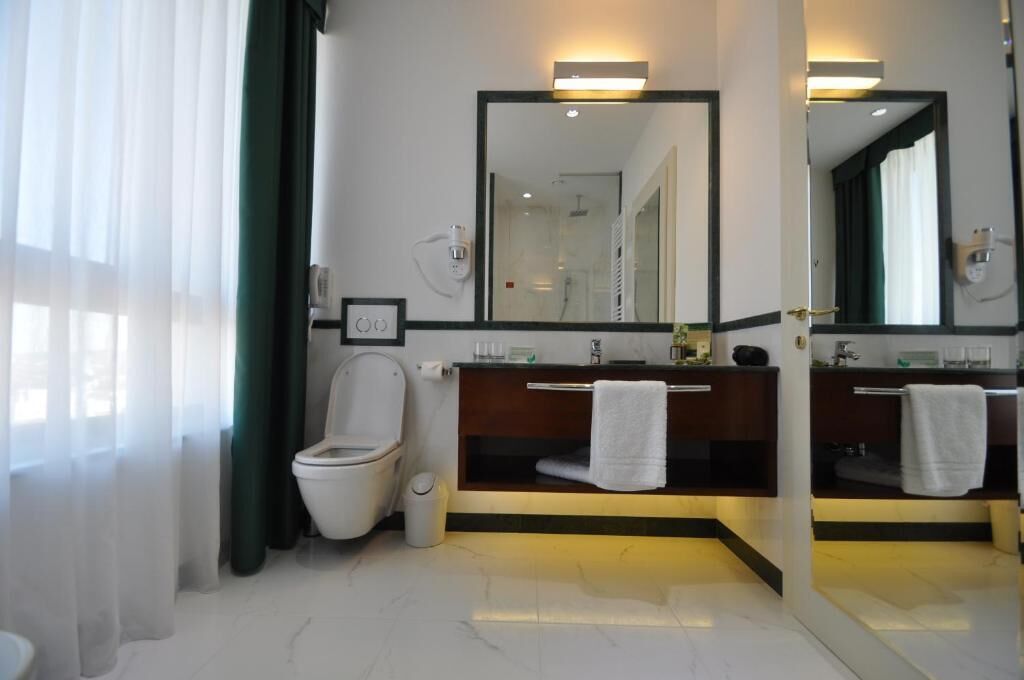 Un baño moderno con inodoro, dos lavabos, un espejo grande y cabina de ducha.