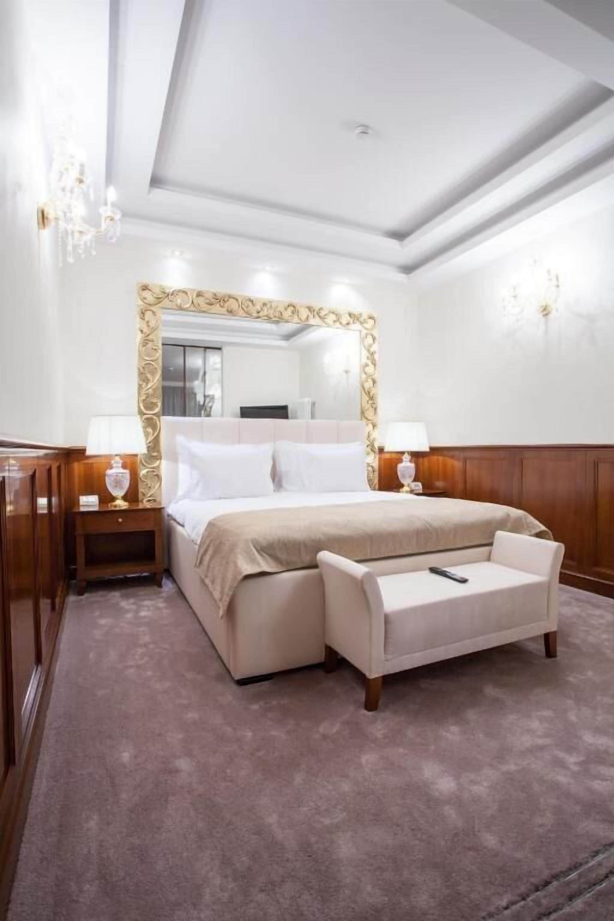 A hotel room with a large bed, two bedside tables with lamps, a large mirror, and a small sofa.