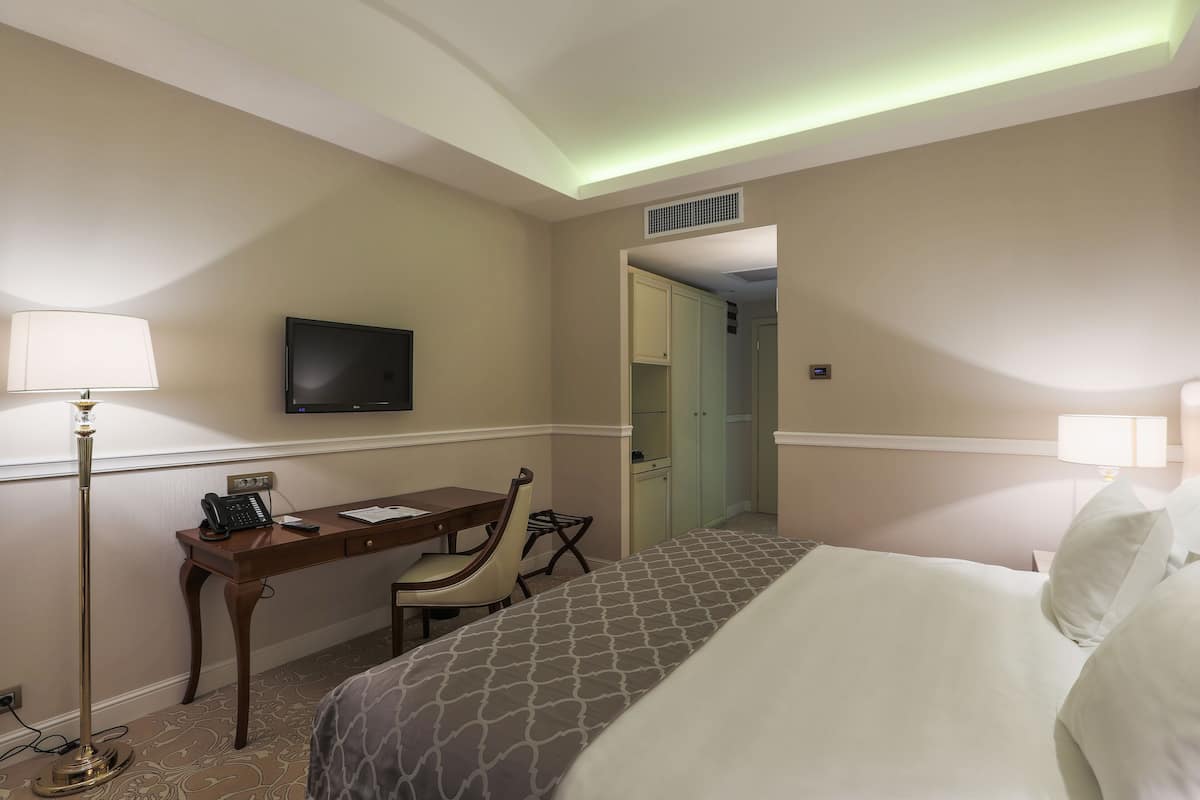 Een hotelkamer met een bed, bureau, stoel, televisie en een lamp.