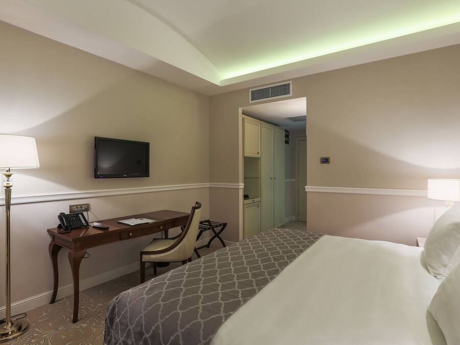 A hotel room with a bed, desk, chair, TV, and a lamp.