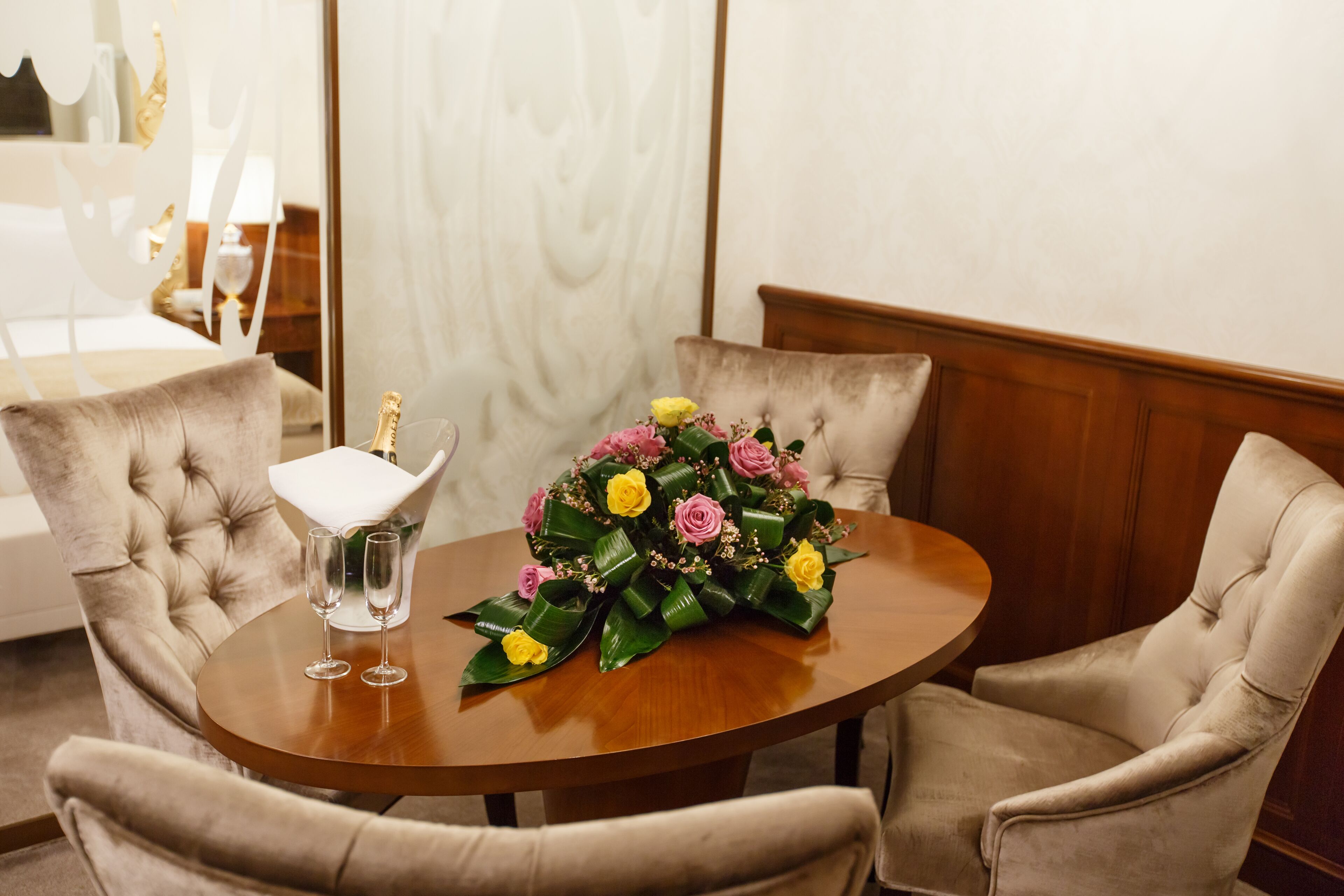A round wooden table with a floral centerpiece and two champagne flutes.