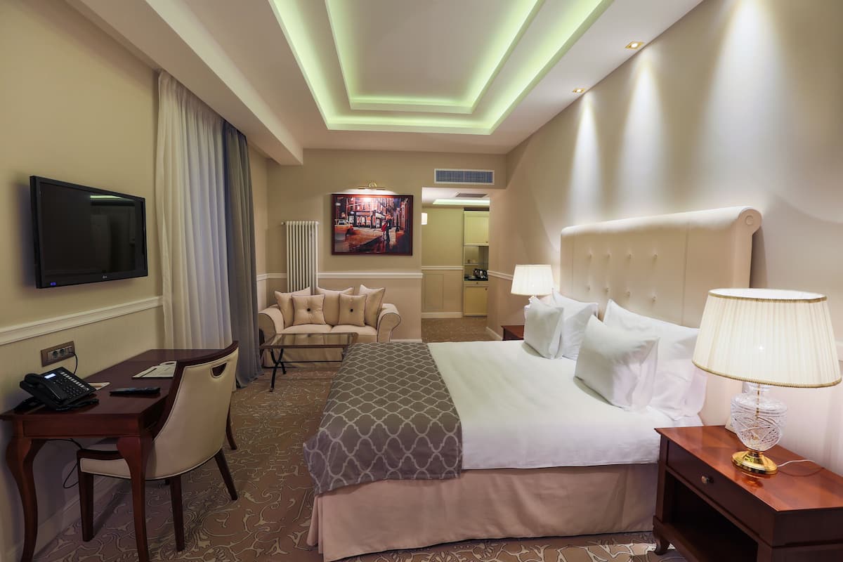 Een hotelkamer met een bed, nachtkastje, lamp, televisie, bureau, stoel en een schilderij aan de muur.