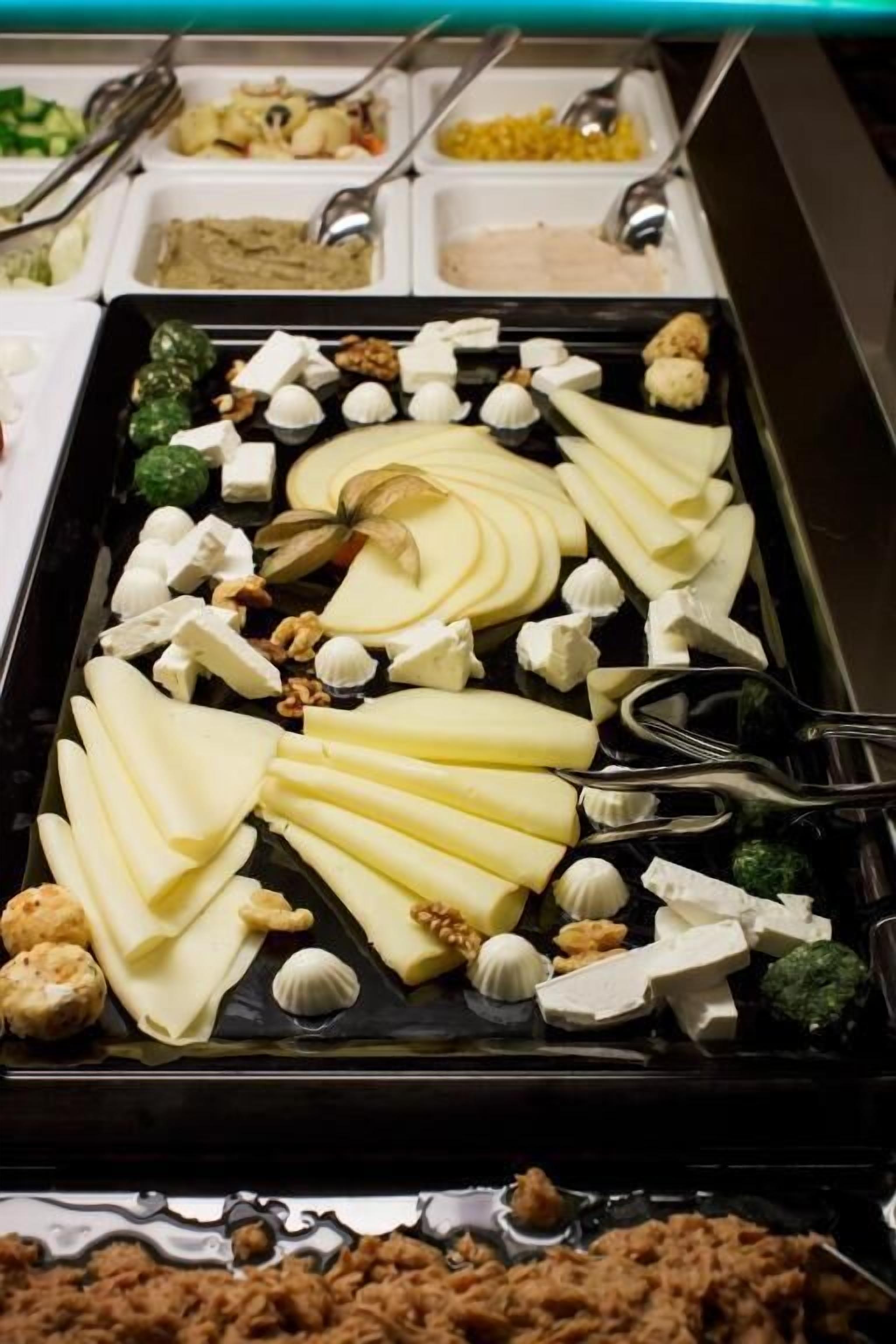 Un bufé con distintos alimentos, incluyendo queso, frutos secos y verduras.