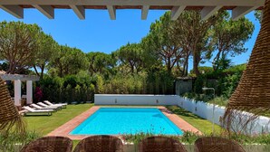 A swimming pool with lounge chairs, a pergola, and lush greenery.