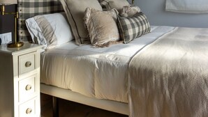 A neatly arranged bedroom with a checkered headboard, multiple pillows, a bedside table with a lamp, and a window with blinds.