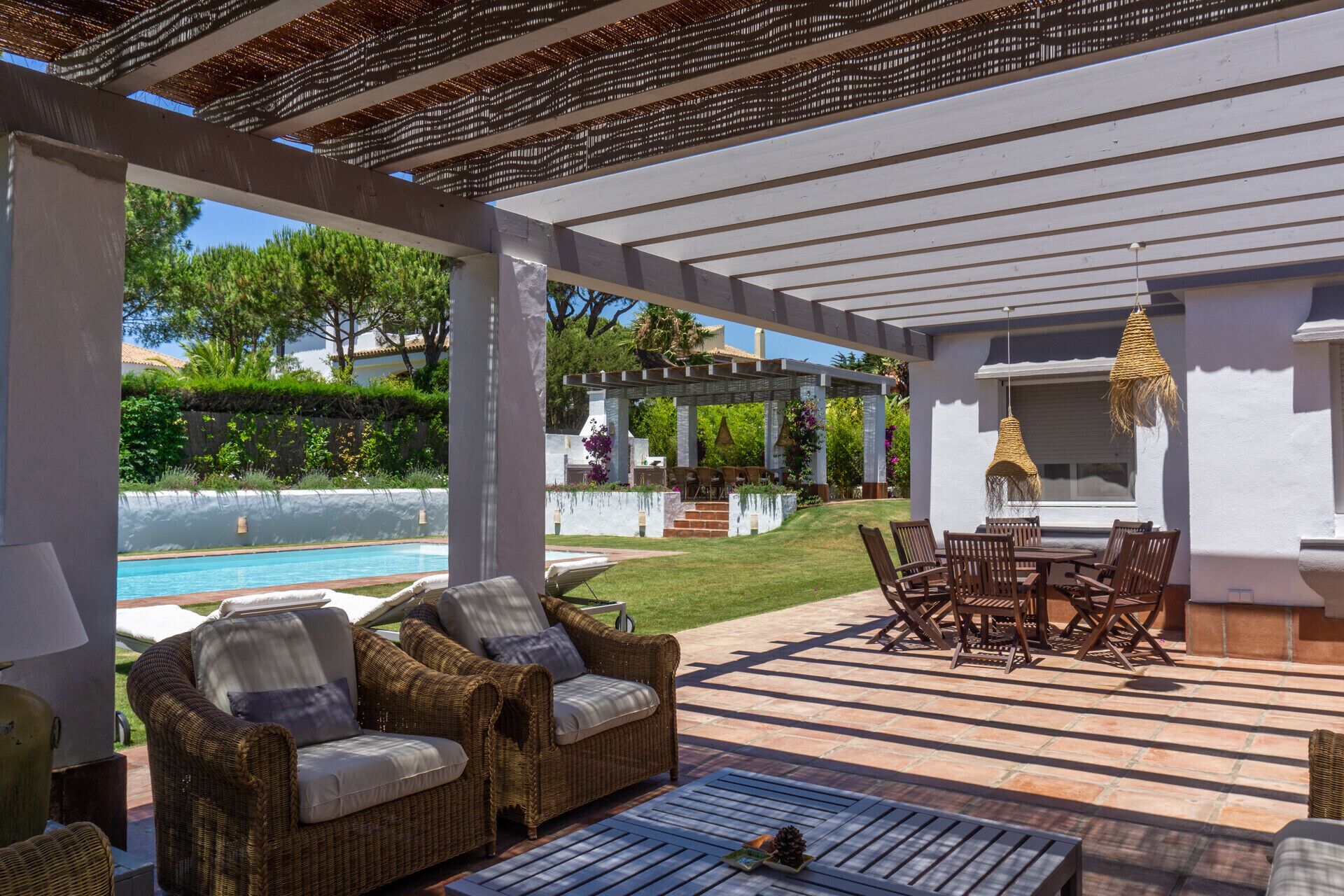 Terrassa exterior coberta amb mobiliari de vimet, una piscina i una pérgola.