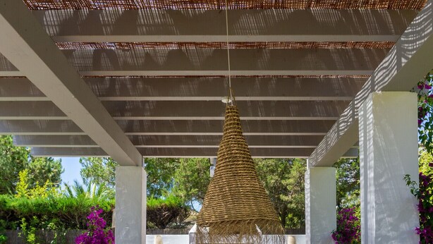 An outdoor patio with a round table and wicker chairs, a hanging light fixture, and a brick fireplace.