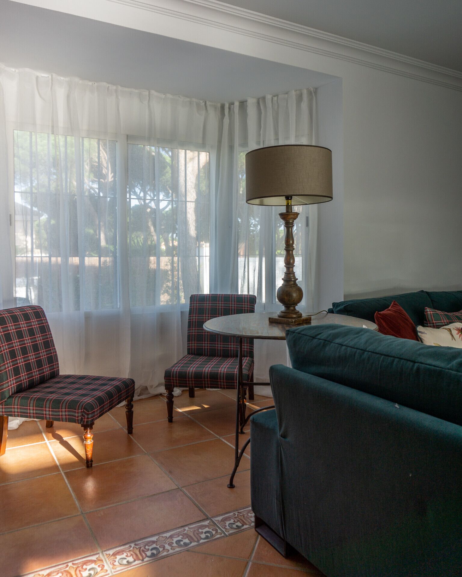 A living room with a green sofa, plaid armchair, and a small table with a lamp.