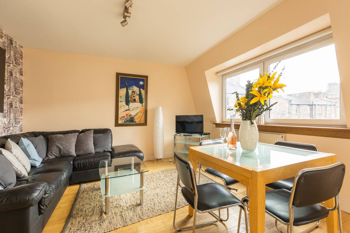 Una sala de estar moderna con una mesa de comedor de vidrio, un sofá de cuero negro y un cuadro en la pared.