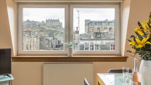 A room with a large window overlooking a historic castle and cityscape. - Amazing Castle View Apartment (Edinburgh)
