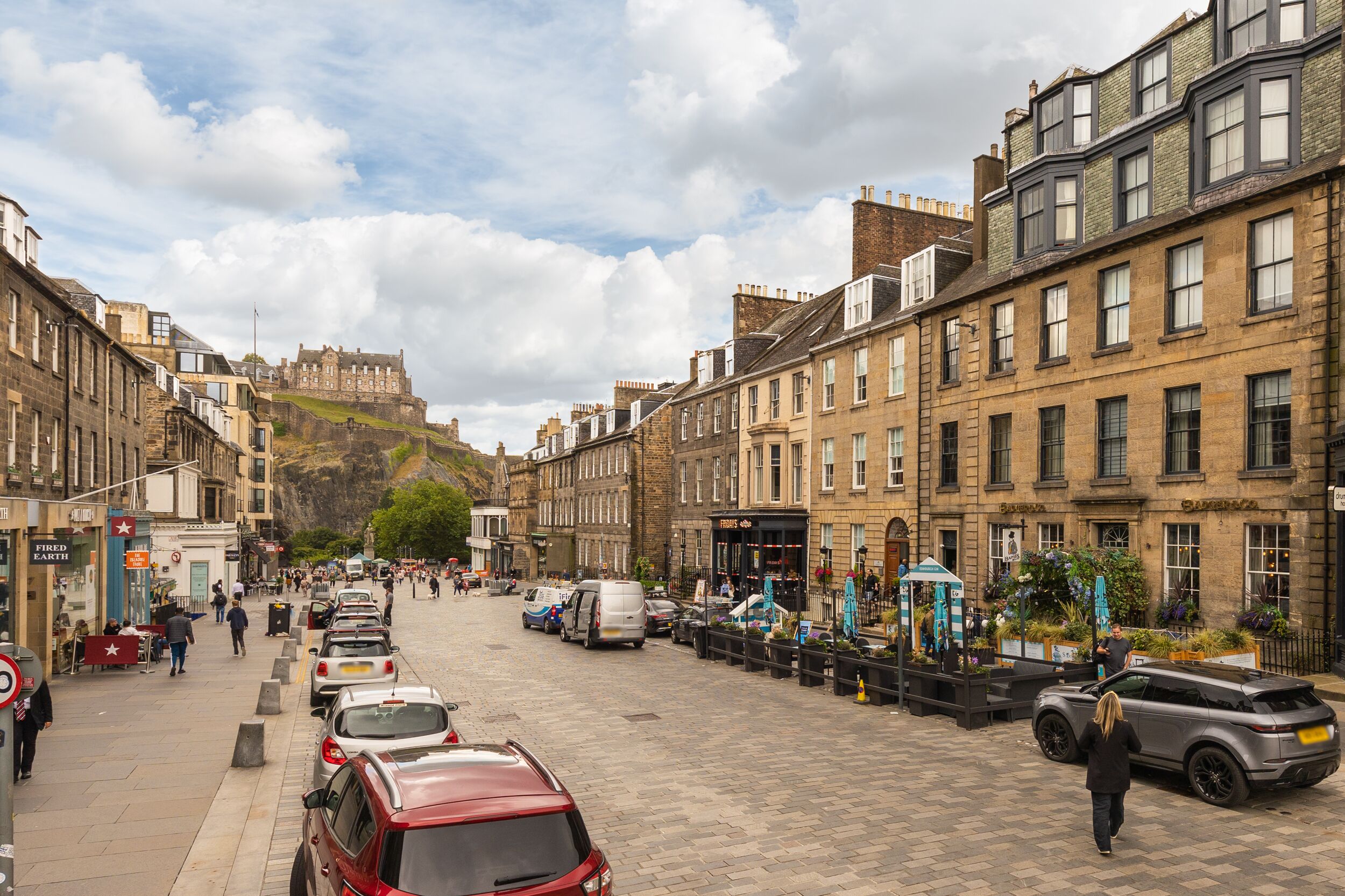 A cobblestone street lined with historic buildings and a castle in the background.
