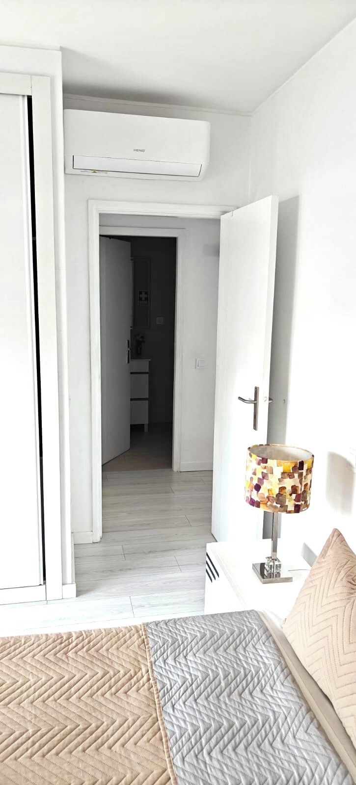 A bedroom with a bed, a bedside lamp, and a door leading to another room.