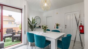 A dining area with a white table, teal chairs, a hanging light fixture, and a view of the outside balcony. - Paradise Porto apartment with terrace in the center of Porto (Porto)