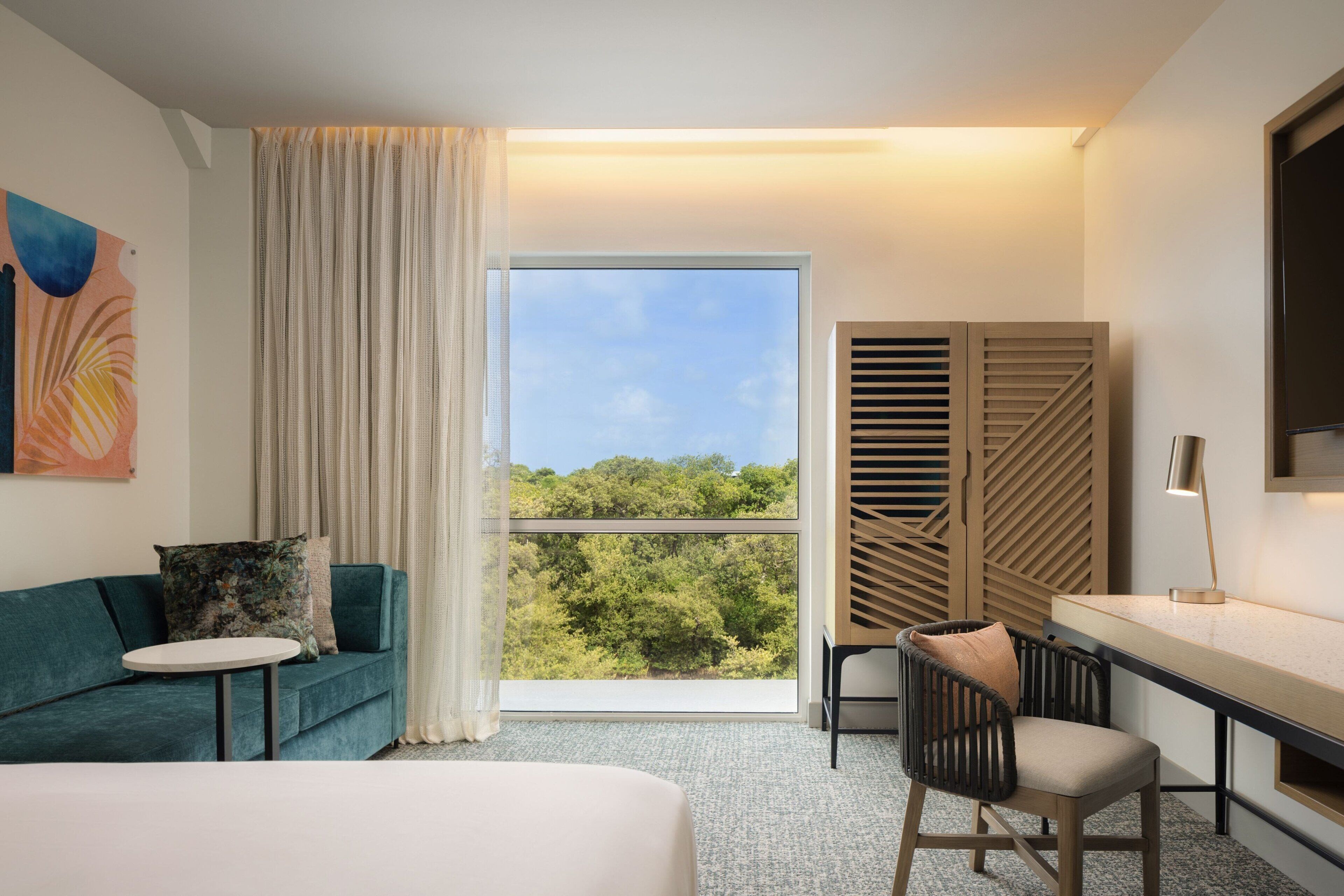 Una habitación de hotel moderna con un ventanal grande, un sofá, un escritorio y una silla.