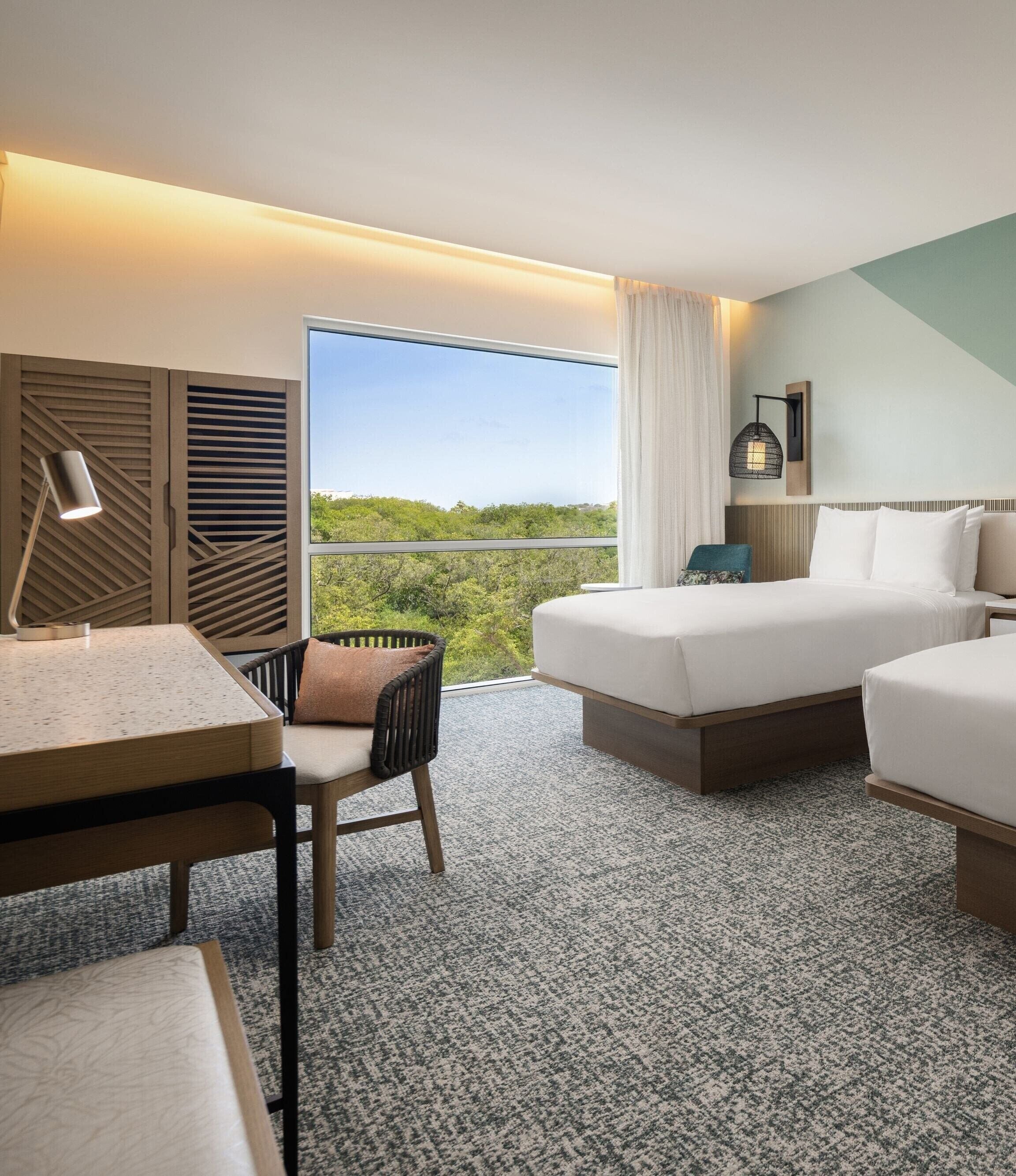 Une chambre d’hôtel équipée d’un lit, d’un bureau, d’une chaise et offrant une vue sur l’extérieur.