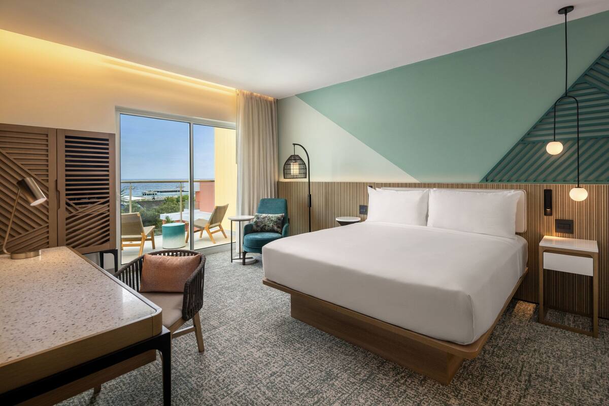 Ein Hotelzimmer mit einem großen Bett, einem Schreibtisch, einem Sessel, einem kleinen Tisch und Blick aufs Meer.