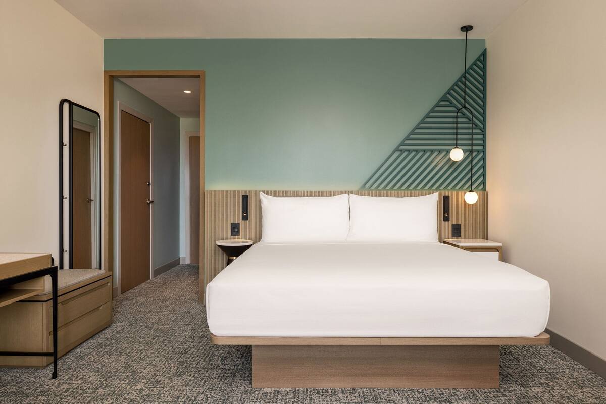 A modern hotel room with a large bed, a desk, and a staircase.