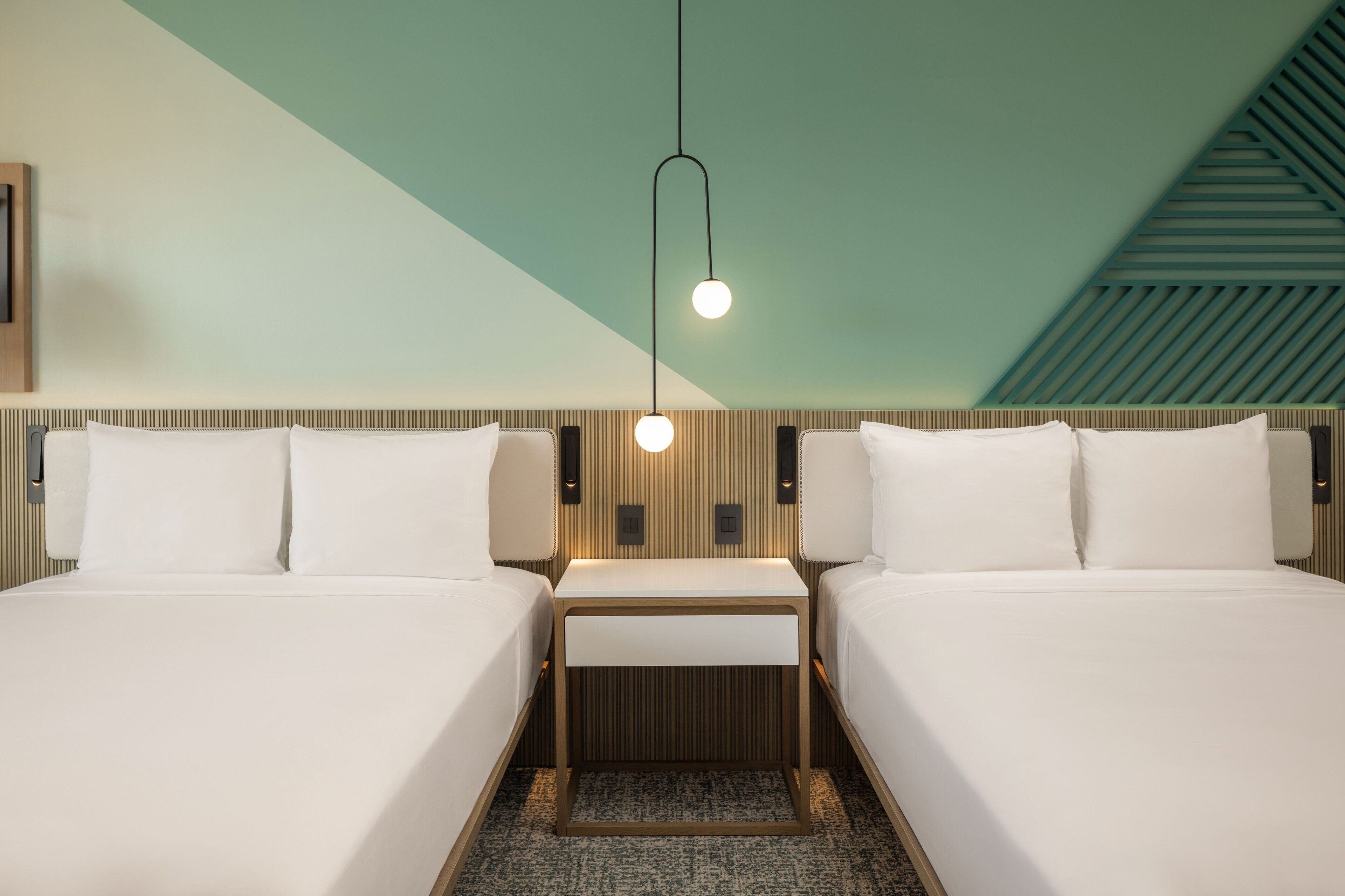 Una habitación de hotel con dos camas, una mesita y una lámpara colgante.