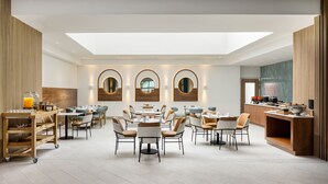 A spacious dining area with multiple tables and chairs, a central serving station, and a skylight above. - Courtyard by Marriott Curacao (Willemstad)