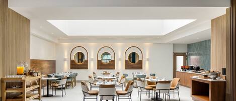 A spacious dining area with multiple tables and chairs, a central serving station, and a skylight above.