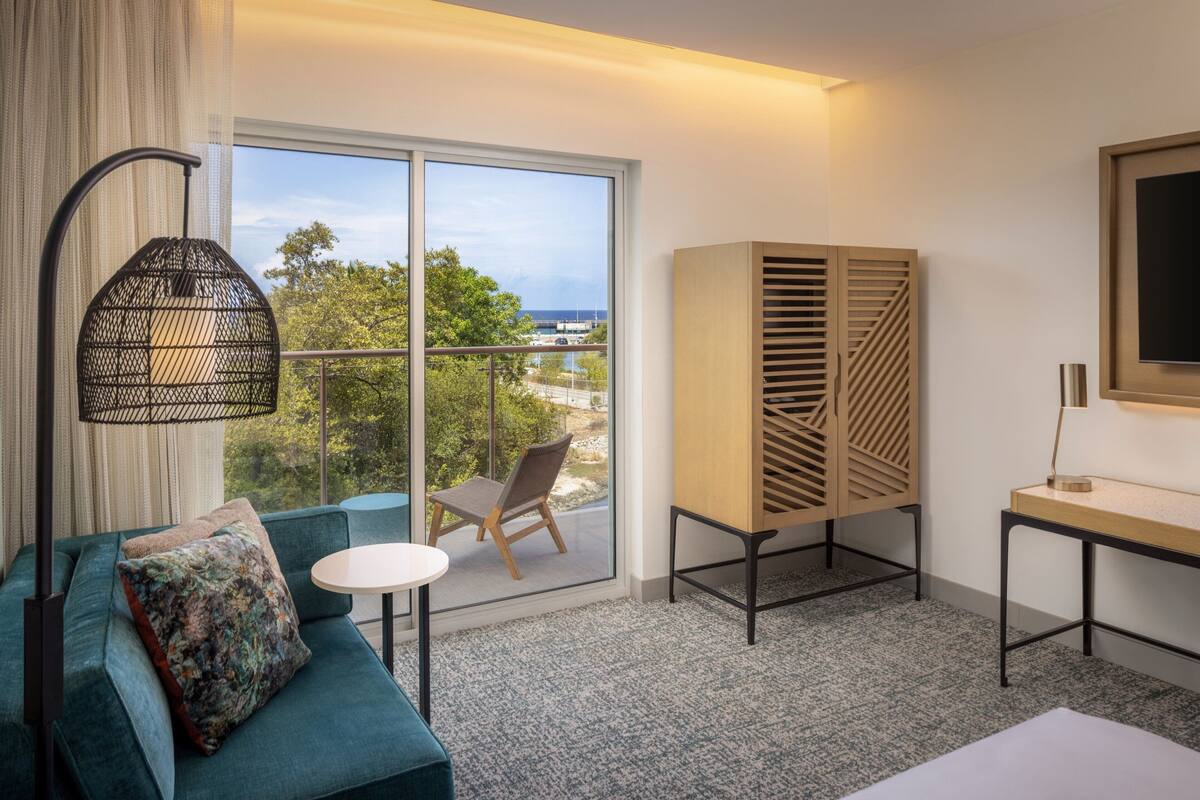 Ein Hotelzimmer mit Balkon, einer Sitzecke, einem Sessel, einem kleinen Tisch und einem Fernseher.
