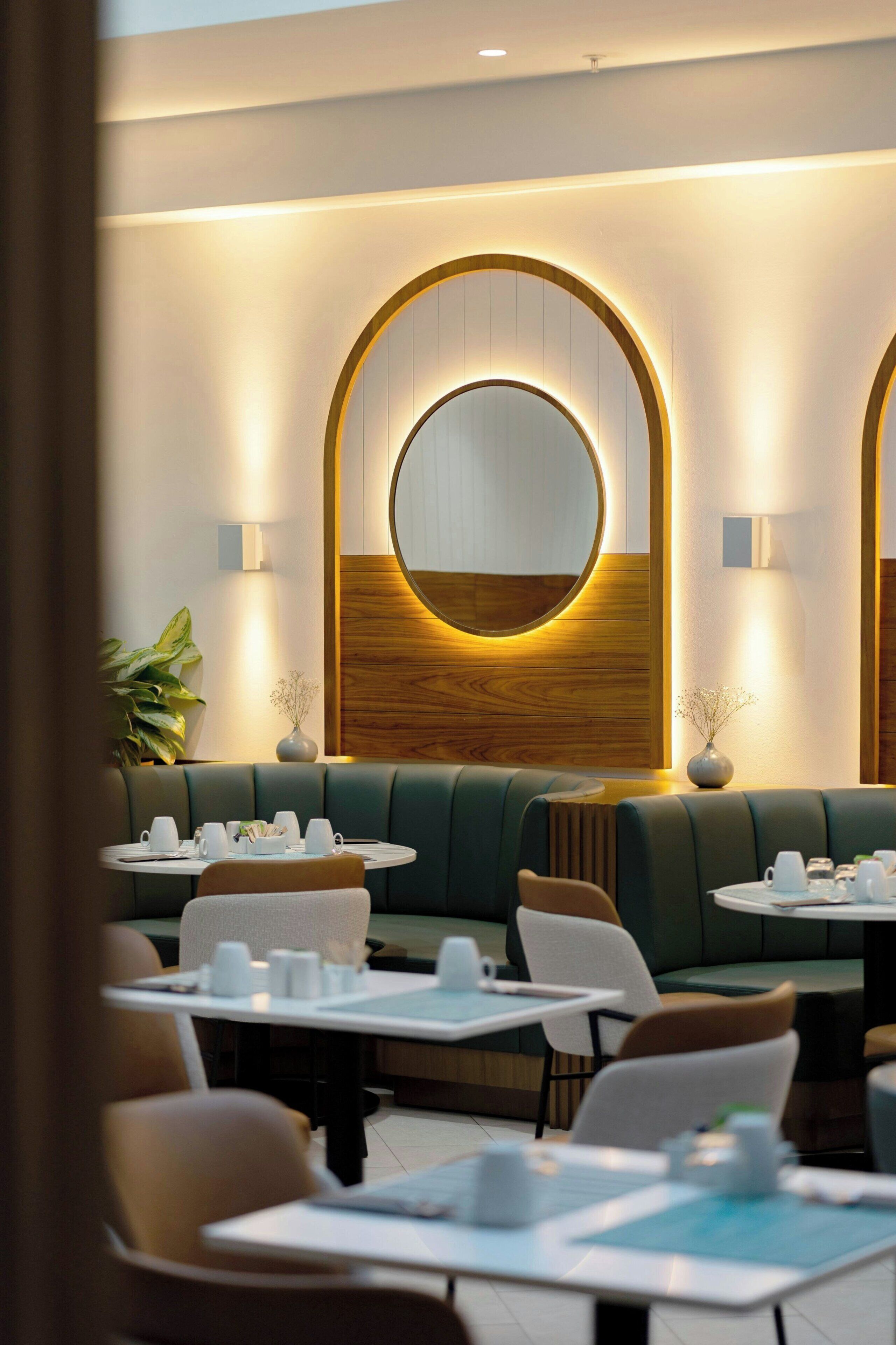 A restaurant with round tables, green booths, and wall-mounted lamps.