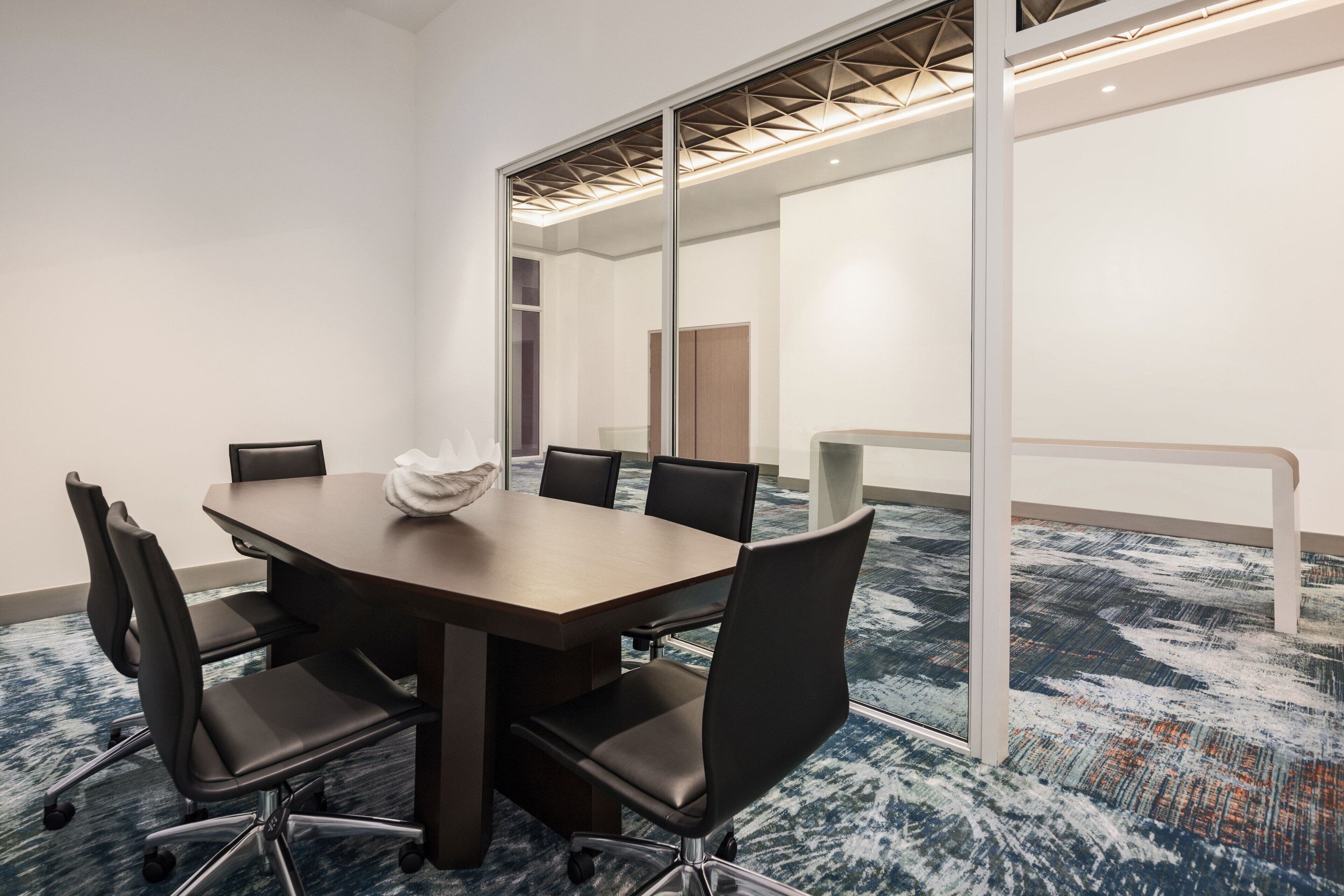 A conference room with a large table, black chairs, and a carpeted floor.