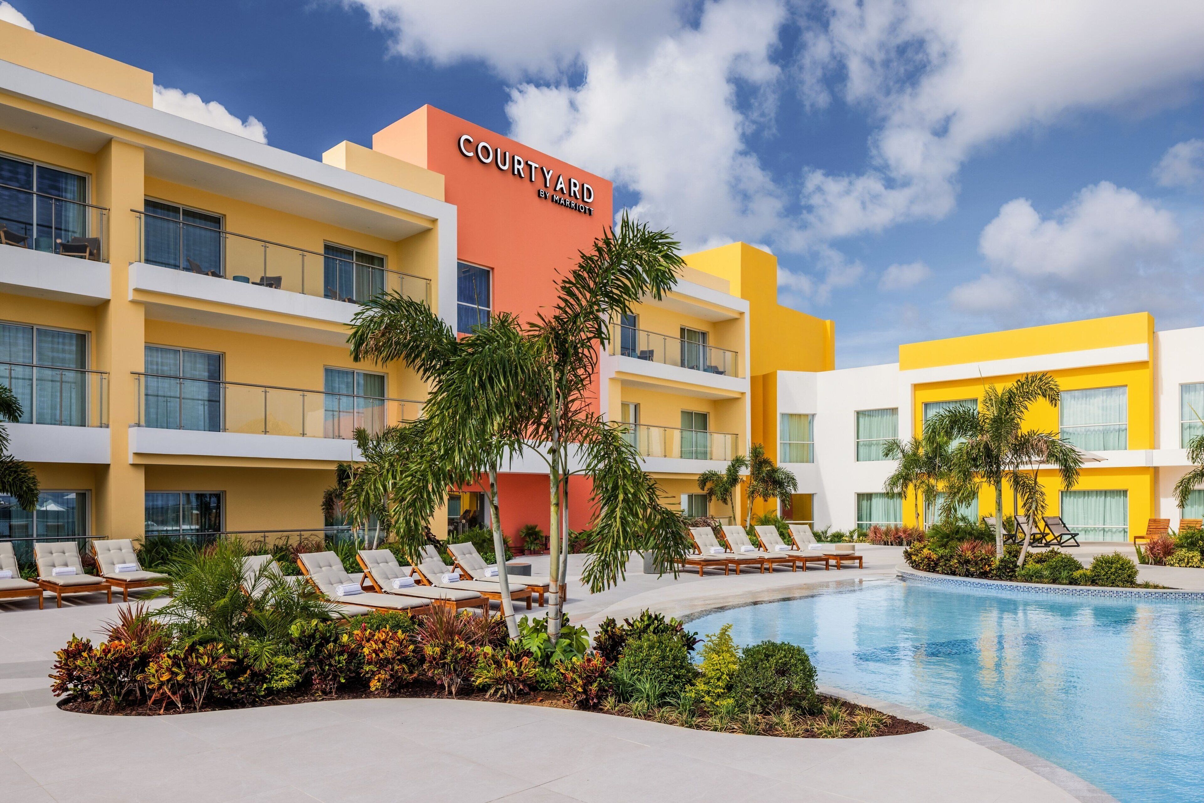 A Courtyard by Marriott hotel with a swimming pool, lounge chairs, and palm trees.