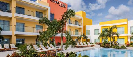 A Courtyard by Marriott hotel with a swimming pool, lounge chairs, and palm trees.