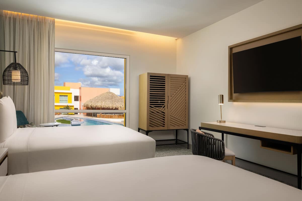 Ein Hotelzimmer mit zwei Betten, einem Schreibtisch, einem Fernseher und Blick auf einen Pool sowie Gebäude.