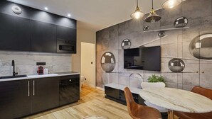 A modern kitchen with dark cabinetry, a built-in oven, and a dining area with a marble table and leather chairs. - Meslay 6 - One Bedroom Apartment, Sleeps 4 (Paris)