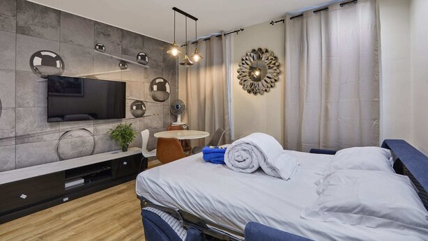 A modern bedroom with a bed, a TV mounted on the wall, a round mirror, and a small table with a chair. - Meslay 6 - One Bedroom Apartment, Sleeps 4 (Paris)