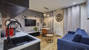 A modern kitchen with a built-in TV, a red appliance, and a sink. There is a dining area with a round table and chairs. A blue sofa is in the living area. - Meslay 6 - One Bedroom Apartment, Sleeps 4 (Paris)
