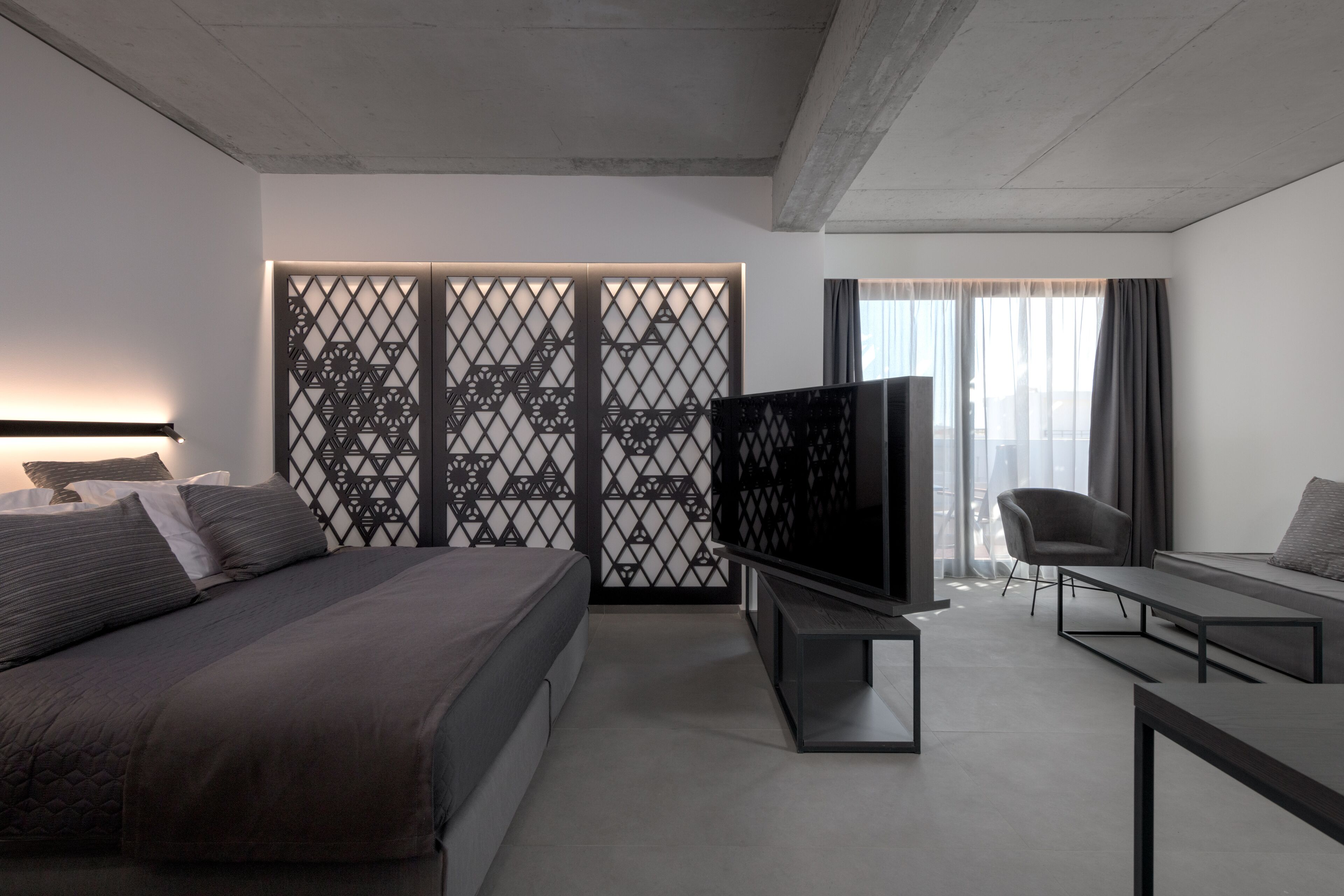A modern hotel room with a bed, a TV, a sofa, and a desk.