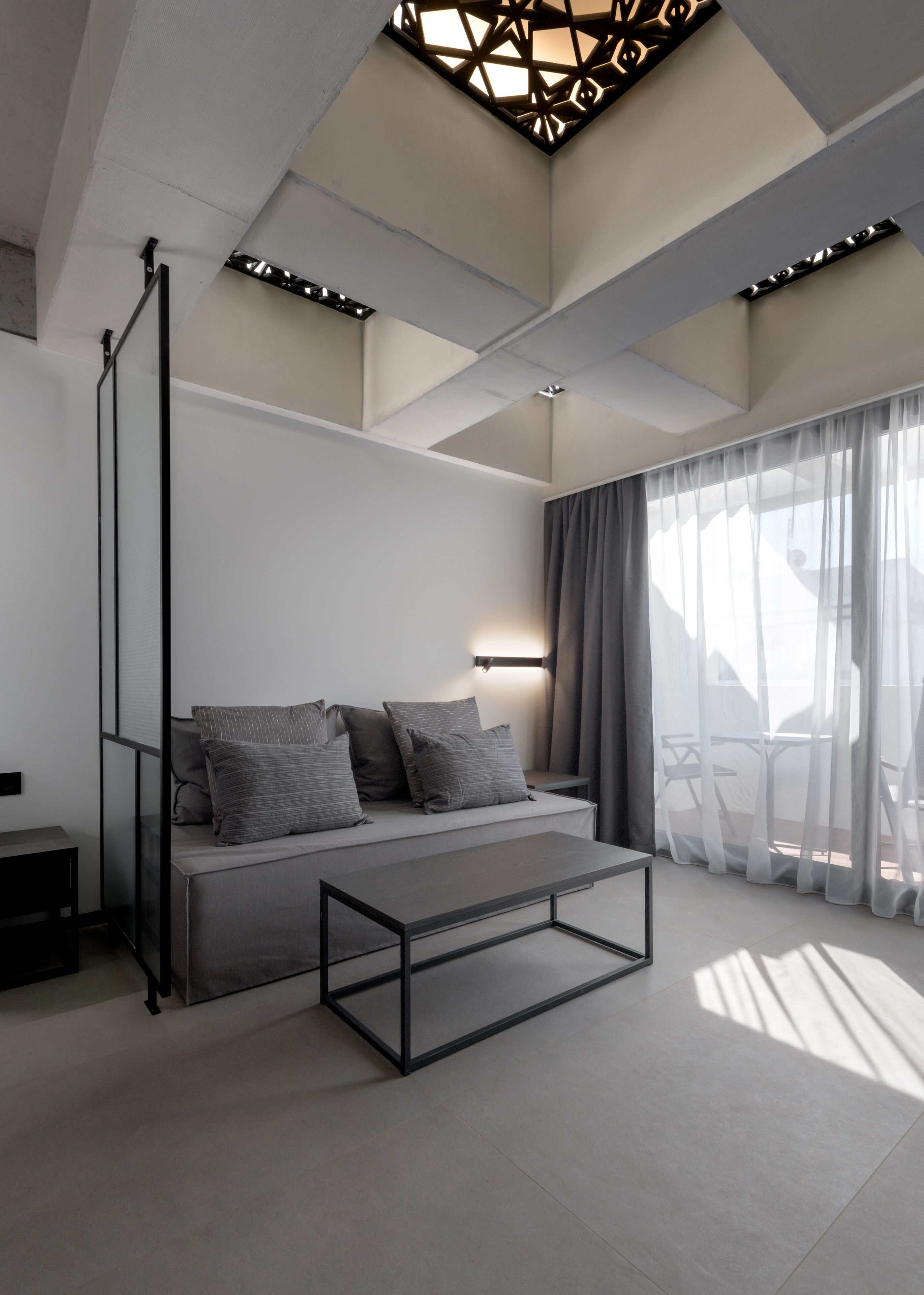 Una habitación moderna y minimalista con sofá, una mesita de centro y un ventanal con cortinas ligeras.