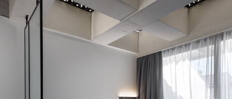 Una habitación moderna y minimalista con sofá, una mesita de centro y un ventanal con cortinas ligeras.