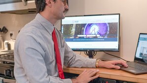 Eine Person sitzt an einem Schreibtisch mit einem Laptop, einem Desktop-Monitor und einem Tablet.