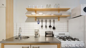 Ett kök med en diskho i rostfritt stål, en kaffebryggare, en brödrost, en spis och köksredskap som hänger på väggen.