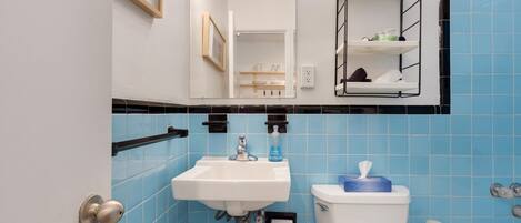 A bathroom with blue tiles, a sink, a toilet, a mirror, and a shelf with toiletries.