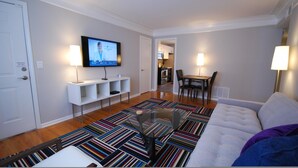 A modern living room with a flat-screen TV, a sofa, a coffee table, and a dining area with chairs and a table. - B2bc Convenient Condo Perfect for Long Term Stay Near Shepherd Center (Atlanta)
