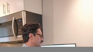 Een persoon in een moderne keuken met roestvrijstalen apparatuur en witte kasten.
